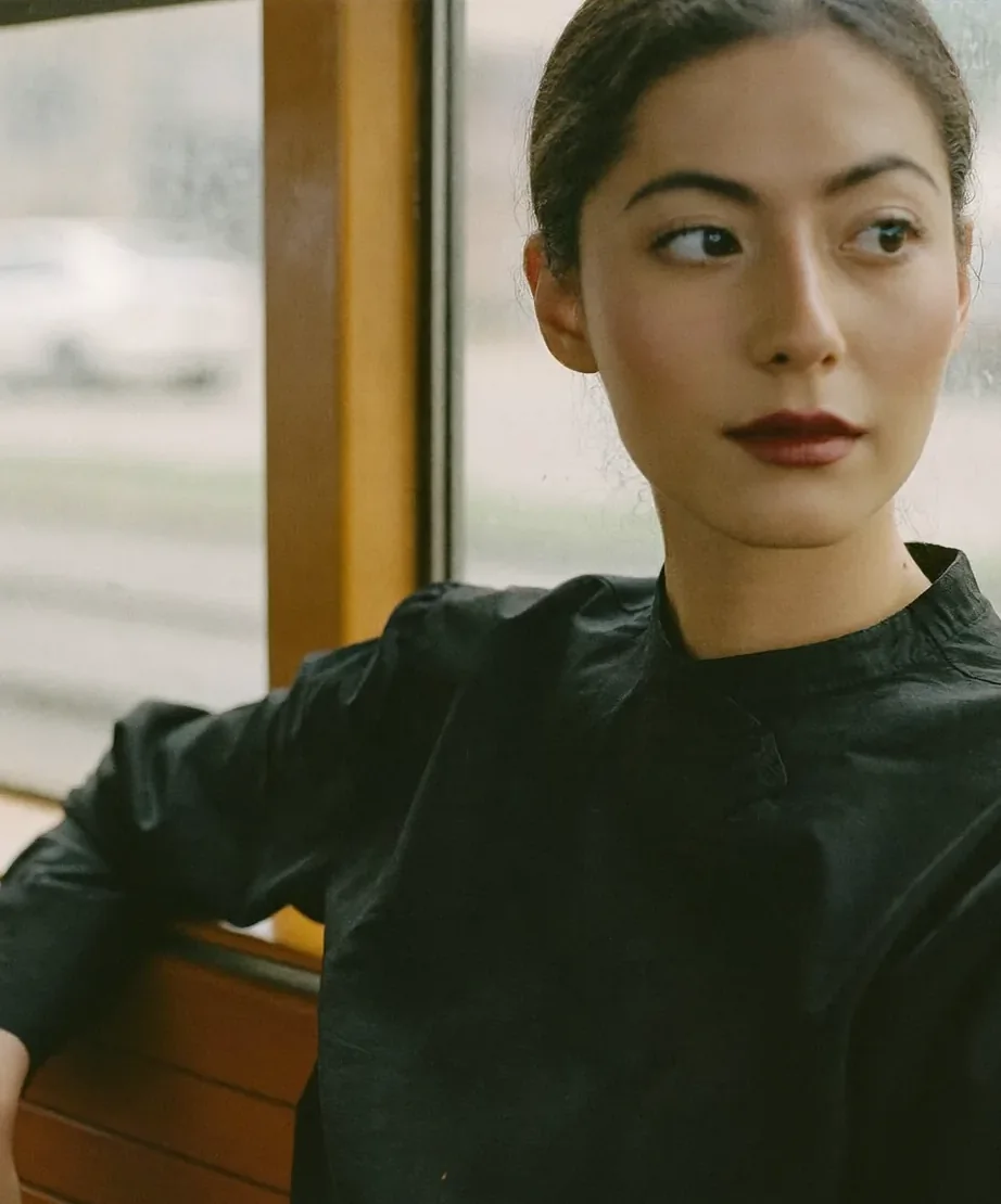 A woman in a black shirt looks away from a tram window, her lips a deep plum