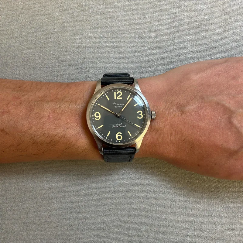 The batch waiter: a large wrist in a black strap, seen from above on a grey cloth