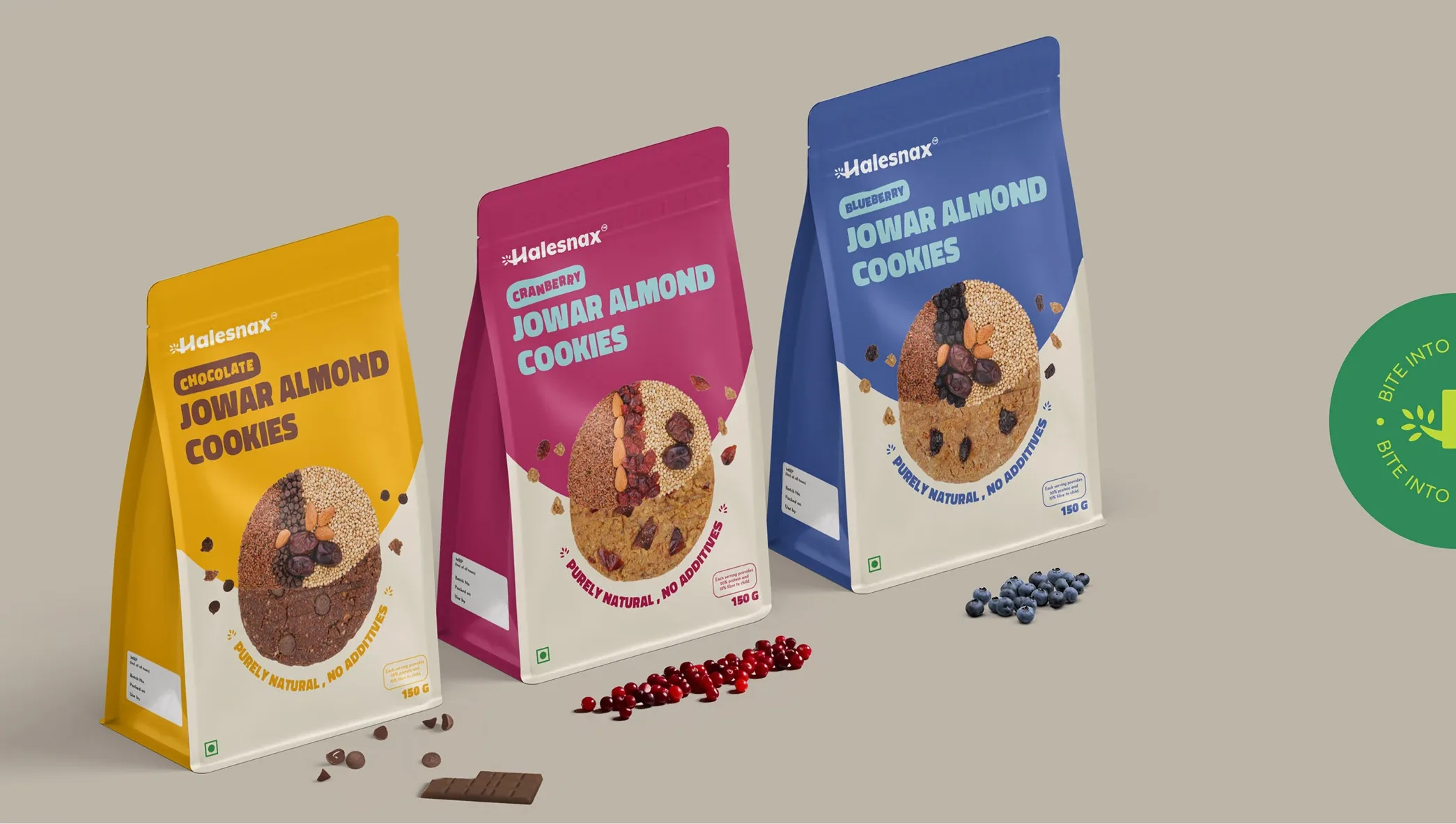 Three cookie pouches, chocolate in yellow, cranberry in crimson and blueberry in blue, lined up with chocolate chips and berries in front