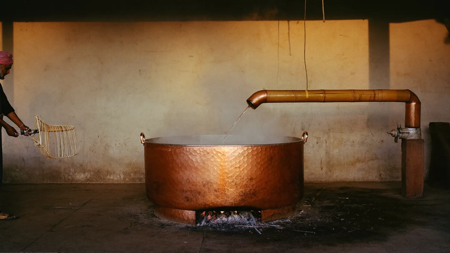 A copper deg over a wood fire in a Kannauj distillery, steam rising in the first light