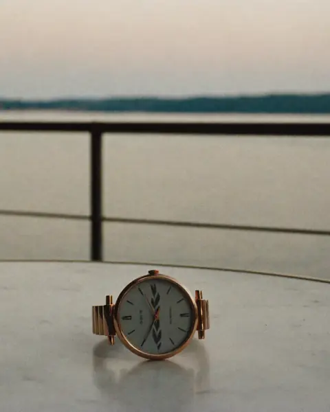 The first-piece buyer: a rose-gold watch on a marble table, a lake and a railing behind it