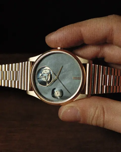 The collector: a hand holds a rose-gold watch on a steel bracelet up to the light