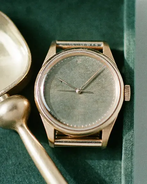 The gift buyer: a rose-gold watch lying on green velvet beside a silver spoon